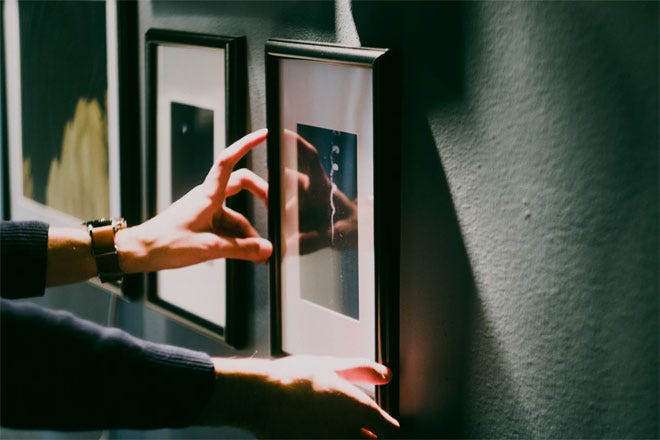 Person hanging up a framed picture on the wall.
