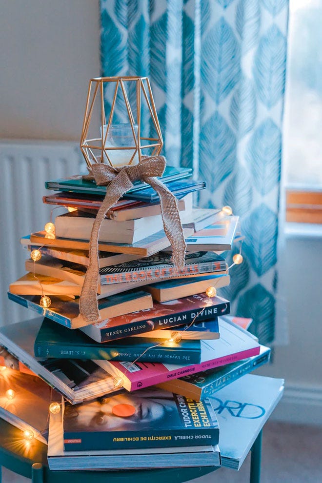 A stack of interesting books on a tabel with a candle on top in front of a white radiator - Hygge | Unsplash.com