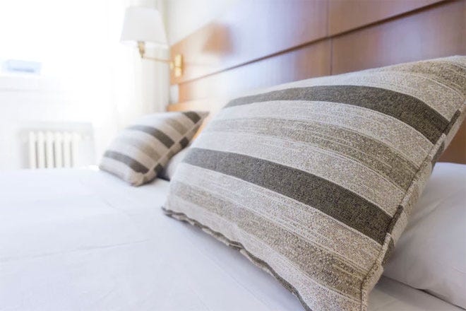 Some stripy throw cushions on a cosy but minimalist white bed with a radiator in the background - Hygge | Unsplash.com