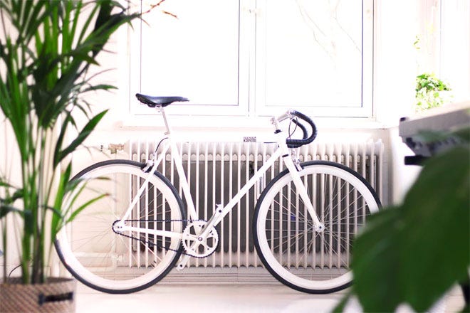 A cool white bicycle leaning against a white cast iron radiator flanked by nice green plants - Hygge | Unsplash.com