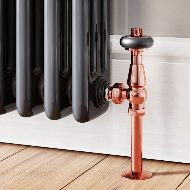 A traditional copper radiator valve with wooden head, connected to a black classic column radiator.