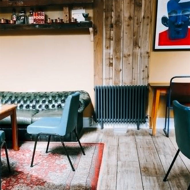 A column radiator in a room next to a green Chesterfield sofa