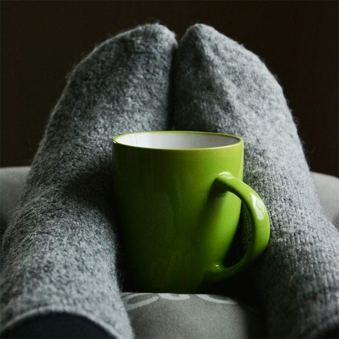 Some feet with thick socks curled around a hot drink
