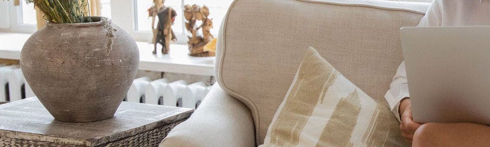 A white column radiator behind a sofa, with a lady sat on it working on a laptop