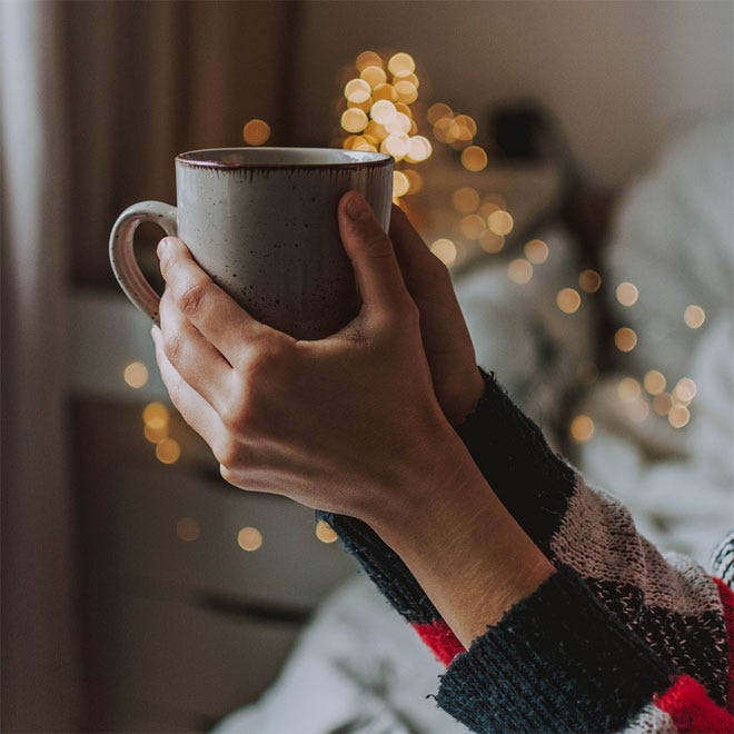 A woman wrapping her hands around a mug containing a hot drink