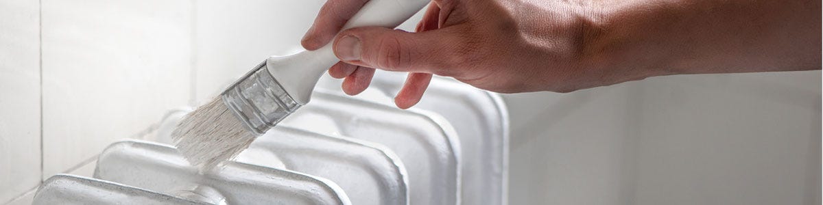 Someone painting a white column radiator with a paintbrush.