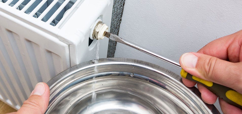 A white panel radiator being bleed of air using a flathead screwdriver